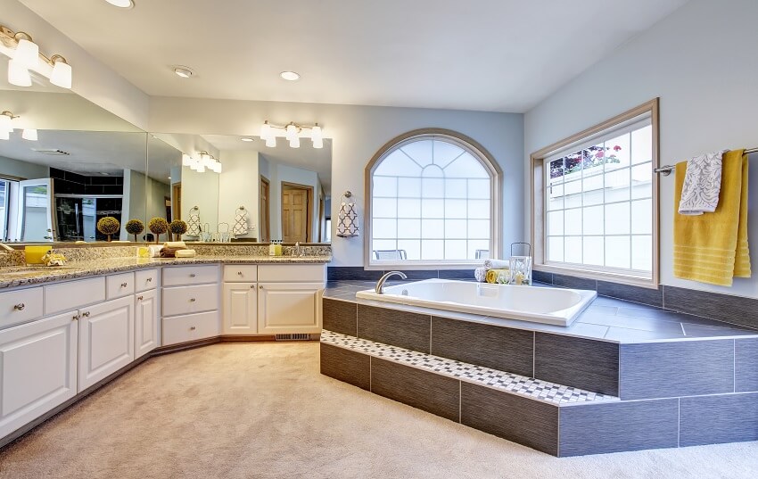 Master bathroom with long vanity, wall lamps, arched window, and step-up drop-in tub