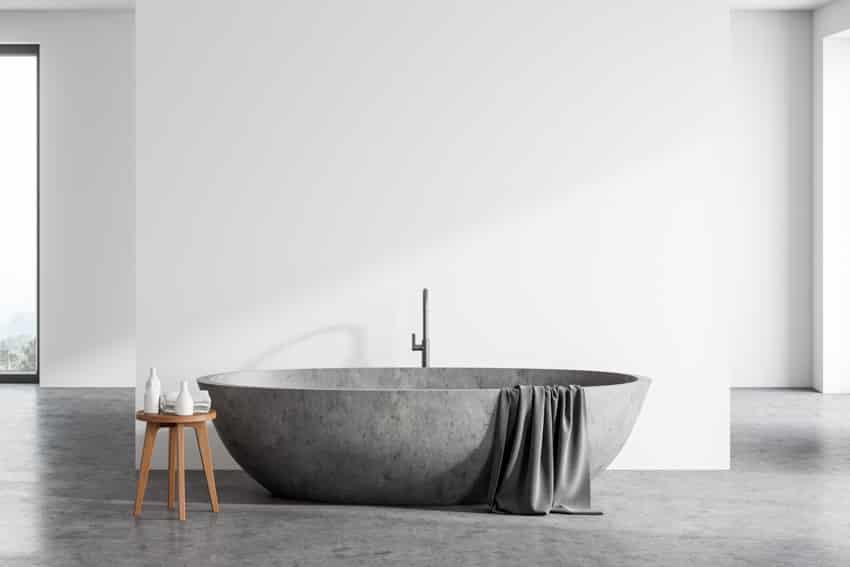 Bathroom with stone bathtub with stool and grey towel