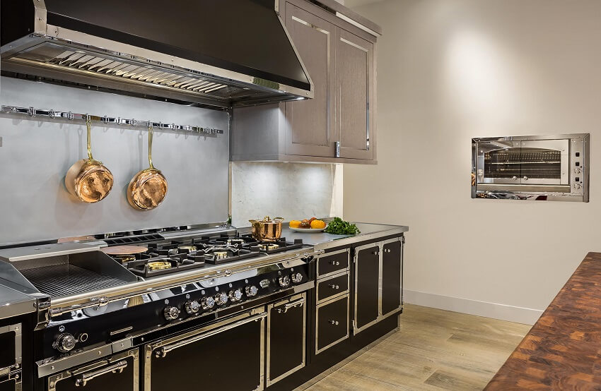 Modern kitchen with wall mounted oven, black cabinets, range hood, and golden kitchenware