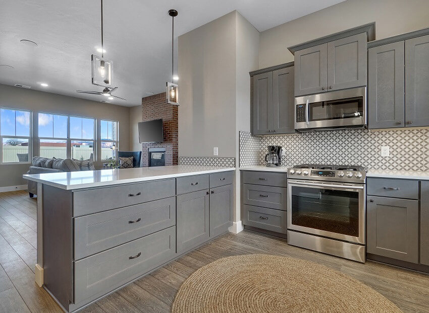 Open kitchen with white countertops, dark grey cabinets, fitted stove, and patterned tile backsplash