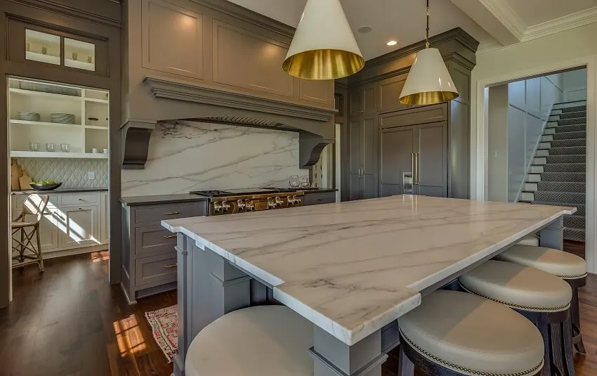 Gray cabinets, marble island countertops and quartz slab backsplash in a kitchen