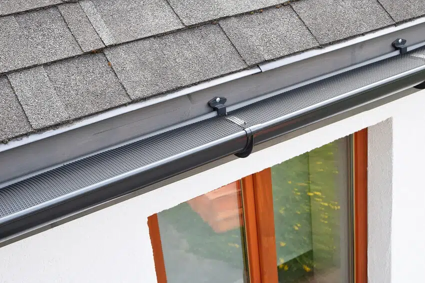 Plastic guard over new dark grey plastic rain gutter on asphalt shingles roof
