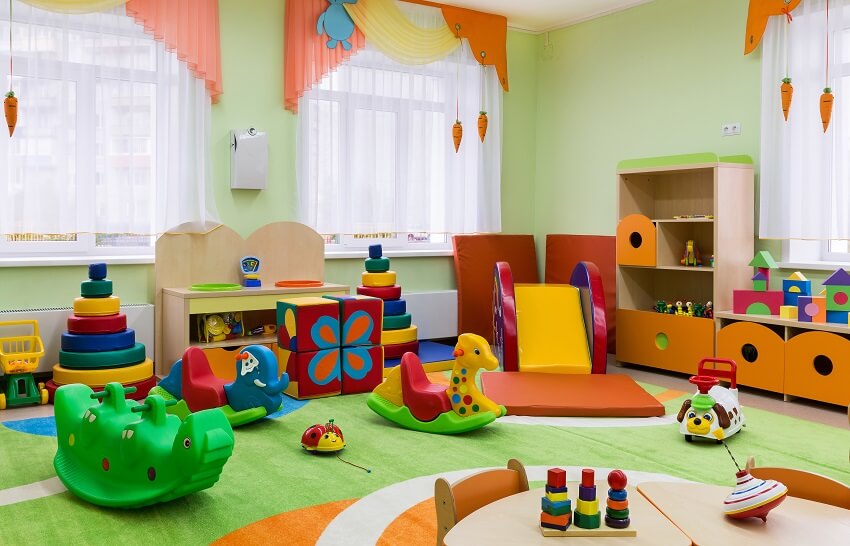 Playroom interior with light green walls, sheer curtains, and wooden toy storage