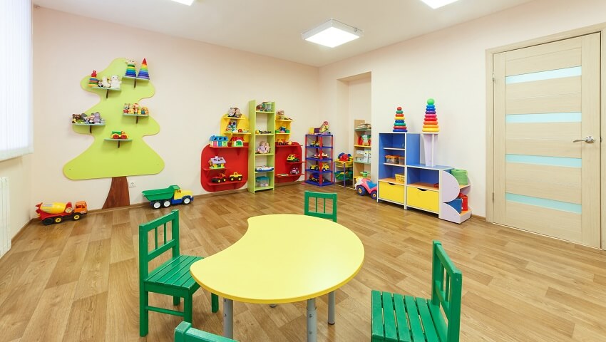 Playroom with neutral walls, wood floor, toys, and a yellow table with green chairs