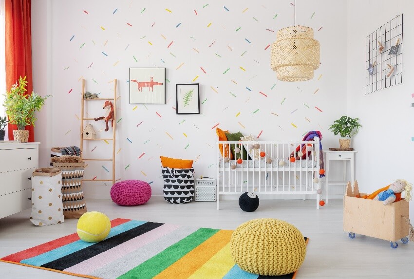 Poufs on colorful rug in baby's bedroom interior with peel and stick wallpaper, lamp, and posters