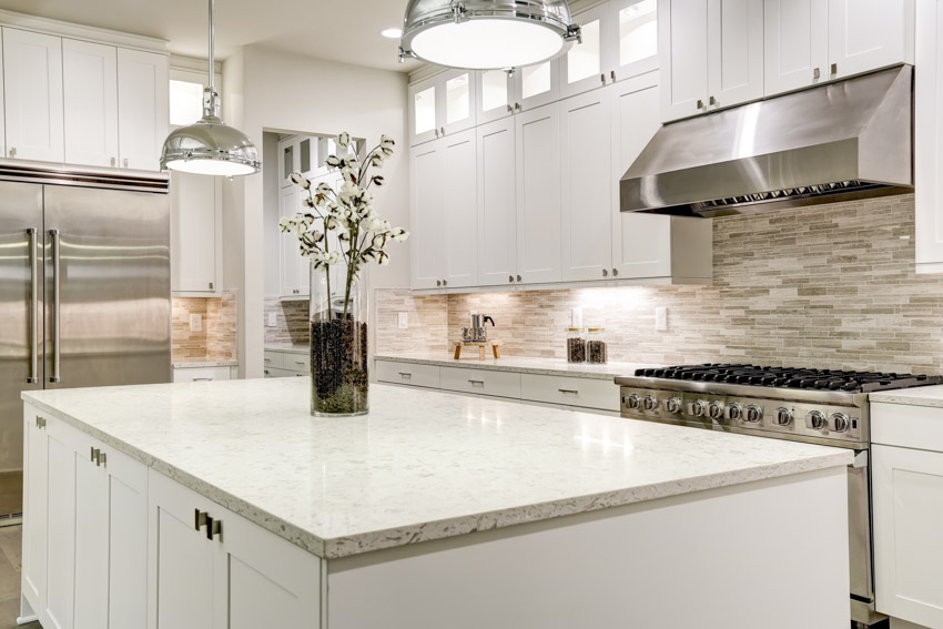 Quartzite countertop on top of island in kitchen with pendant lights, backsplash, and white cabinets