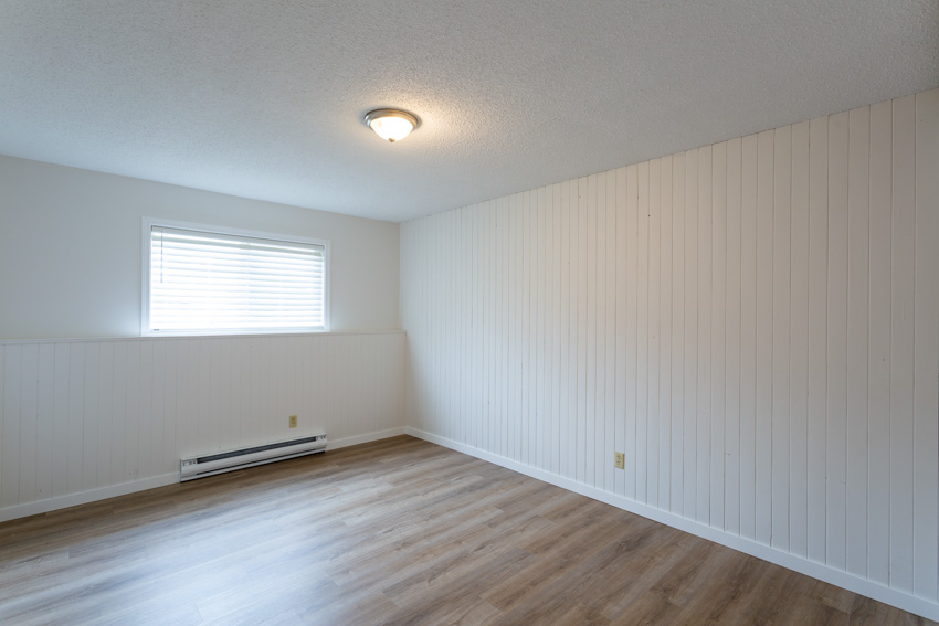 Room with white wood accent wall, electric baseboard heater, ceiling light, wood floor, and ceiling light
