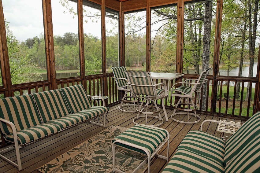 Screened porch on lakeside house with small carpet, striped sofa, and chairs