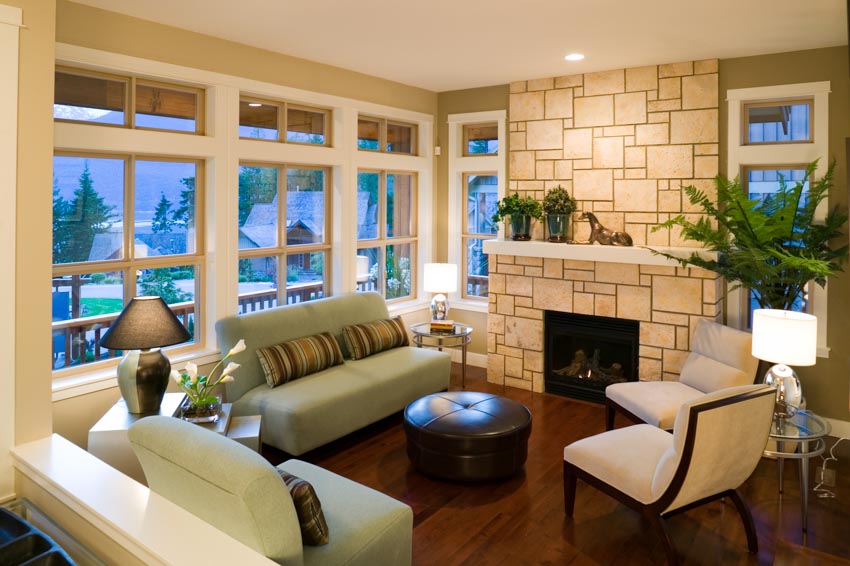 Simple living room with fireplace, couches, chairs, wood flooring, lamps, and windows