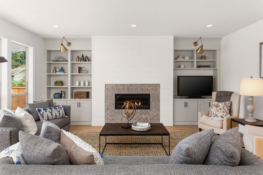 Simple living room with fireplace tile design, recessed lights, shelves, and couches
