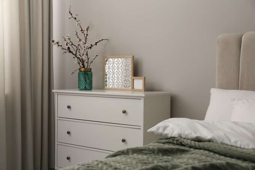 Small guest bedroom with white nightstand, drawers, and window curtain