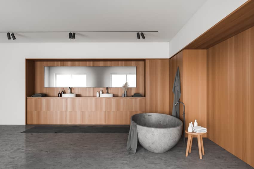 Bathroom with natural stone tub, wood accent wall, track lighting, and concrete flooring