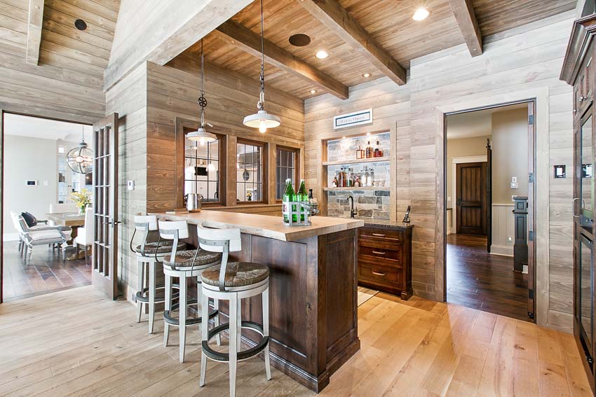 Spacious home bar with high chairs, wet backsplash, pendant lights, and wood flooring