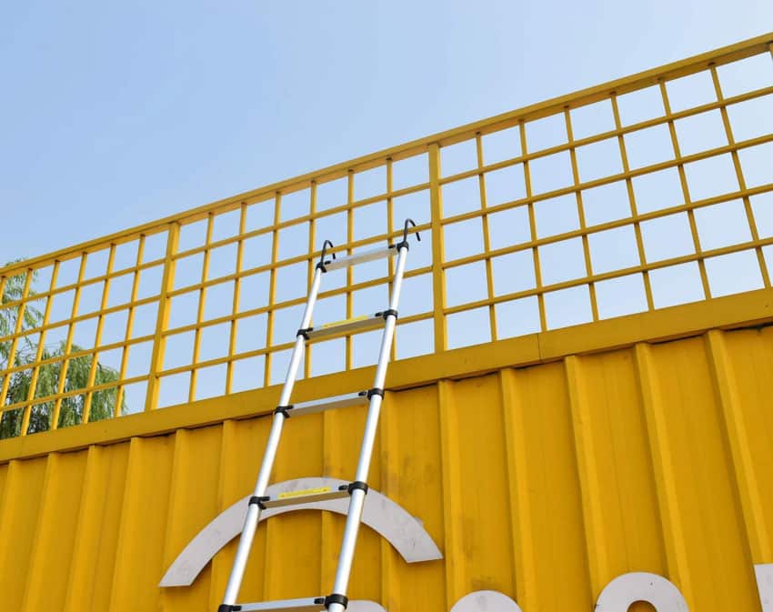 Telescopic ladder on yellow metal fences