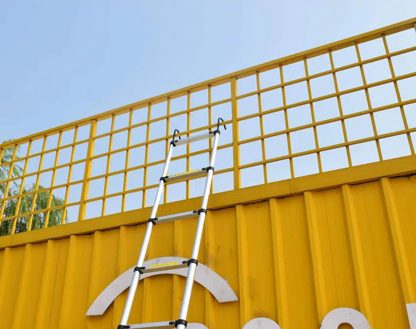Telescopic ladder on yellow metal fence