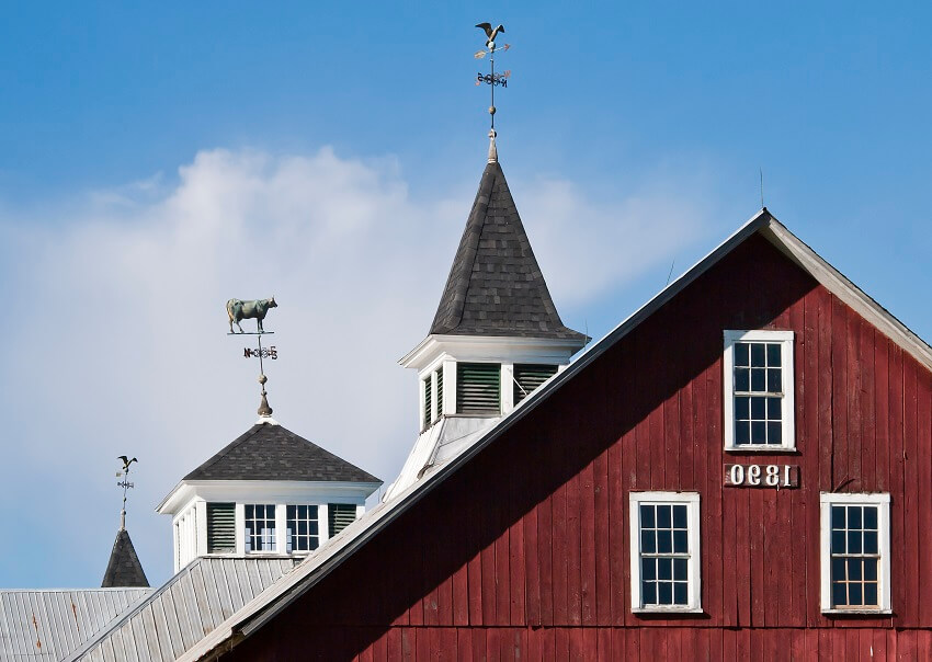 The gable peak and cupola from an old red wooden barn with windows