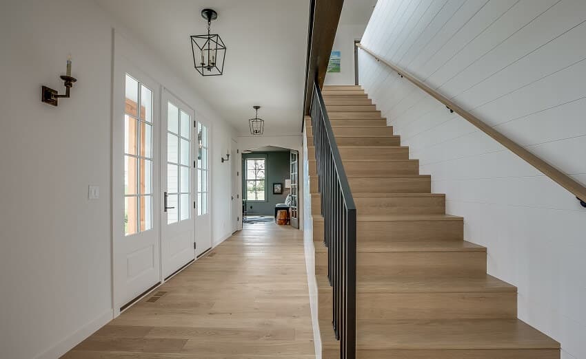 Vinyl flooring on stairs with black railing and white walls, and hallway with lighting fixtures