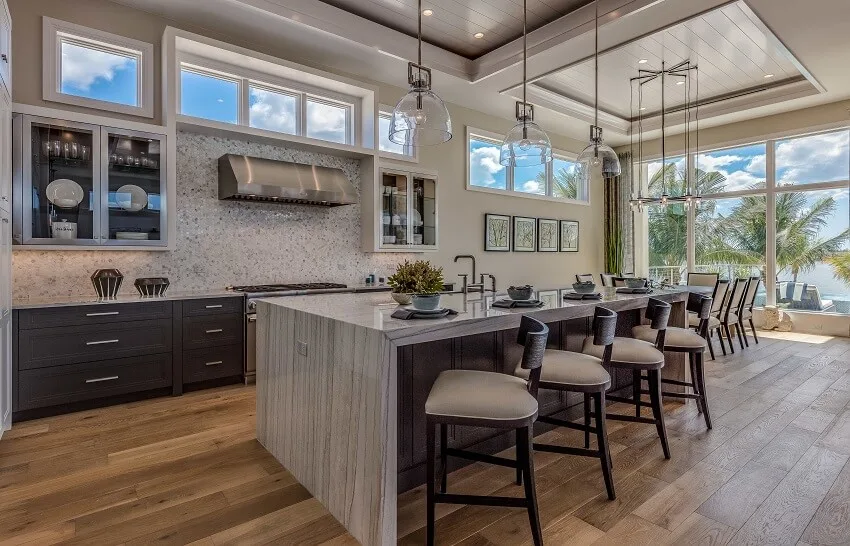 Waterfall quartz countertop island, pearl backsplash, and coffered ceiling in an open kitchen