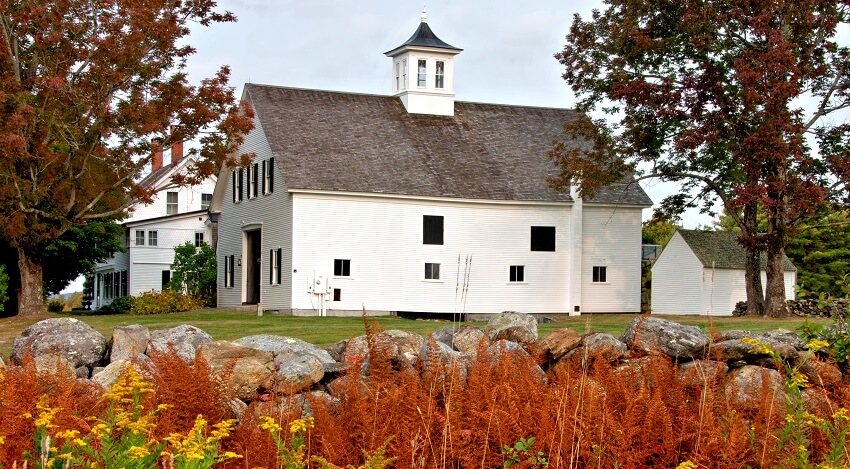 White barn with cupola and bronze colored fern leaves and old stone wall