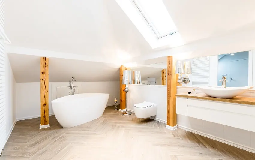 White bathtub and toilet in spacious attic bathroom with skylight window, beams, and mirror