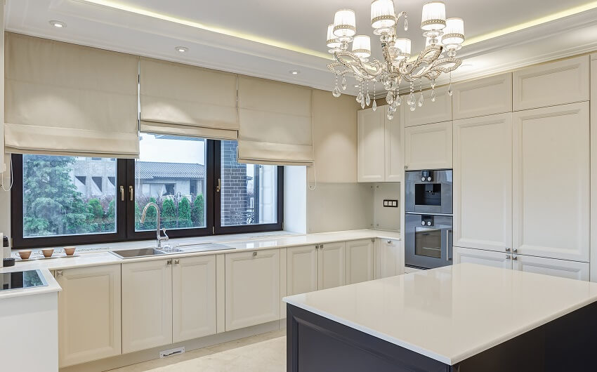 White kitchen with chandelier, marble floor, and windows with shades