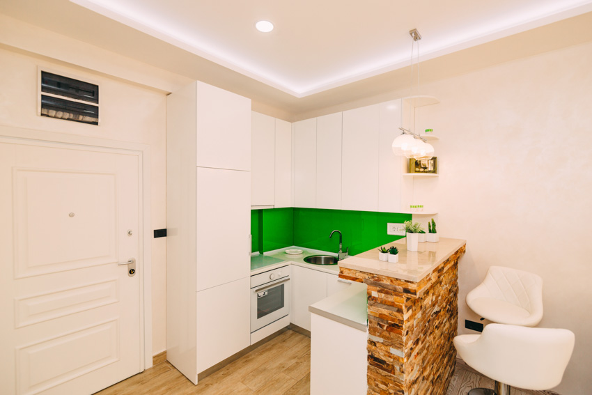 White kitchen with green backsplash as accent wall, cabinets, and recessed lights