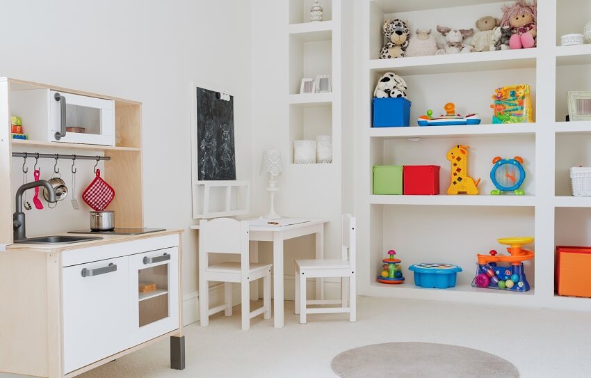 White playroom with built-in shelves storage for toys a mini toy kitchen small table and chairs