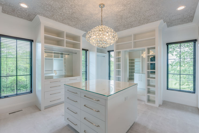 White walk in closet with center island, glass countertop, cabinets, windows, and hanging light