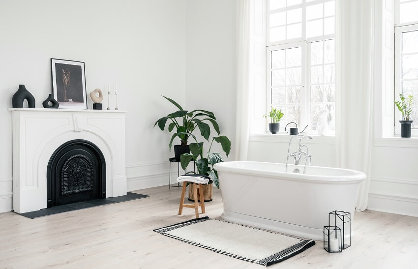 White bathroom with freestanding porcelain bathtub, indoor plants, and decorative fireplace