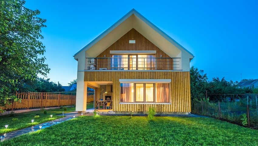 Wooden barndominium with lawn, lighted walkway, porch, and a balcony