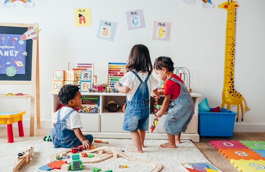 Young children enjoying in the playroom with wall decors, white toy storage, and a carpet