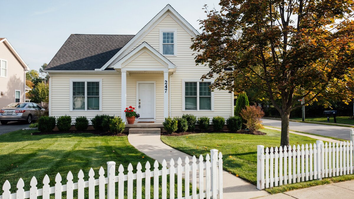 Suburban home behind a wavy white picket fence framing a green front lawn