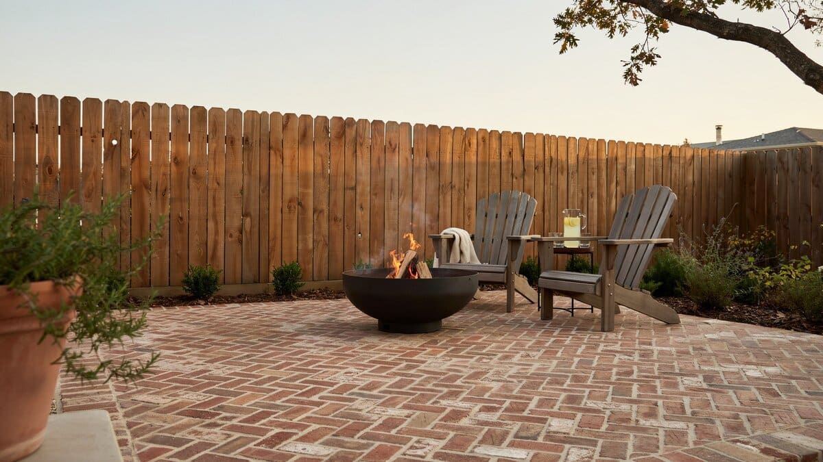 Stockade style wood fence around a brick patio with a fire pit