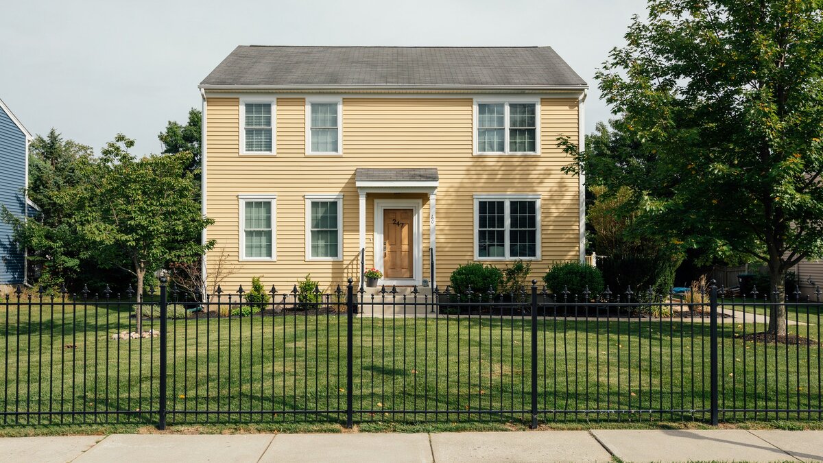 Black metal fence in front of a yellow suburban house
