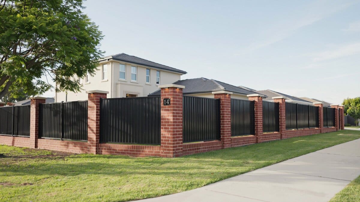 Property fence with brick columns and black metal panels in front of a house