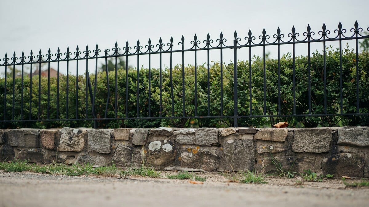 Black wrought iron fence mounted on a stone retaining wall
