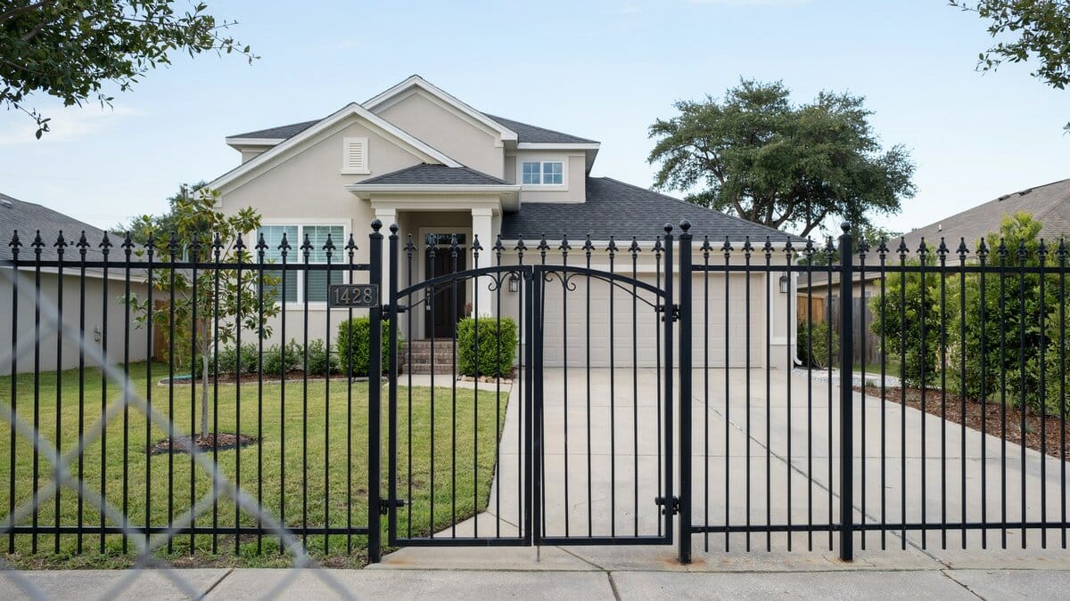 Suburban home behind a wrought iron fence with a double driveway gate