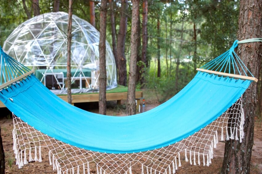 A blue hammock tied to a tree and transparent bell tent in a camp setting in the forest