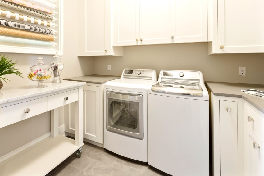 A combined craft and laundry room with white cabinets and a console table