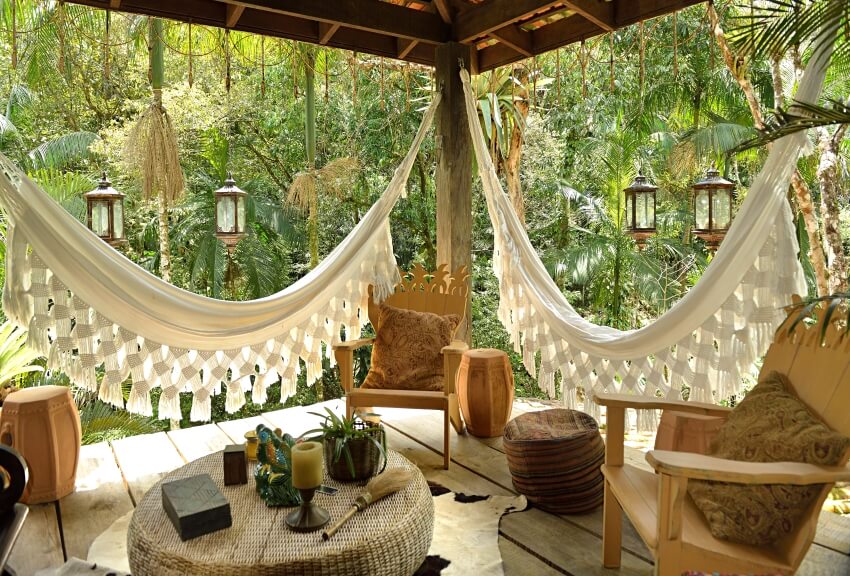 A porch with wood chairs rattan table lamps and white cotton hammocks
