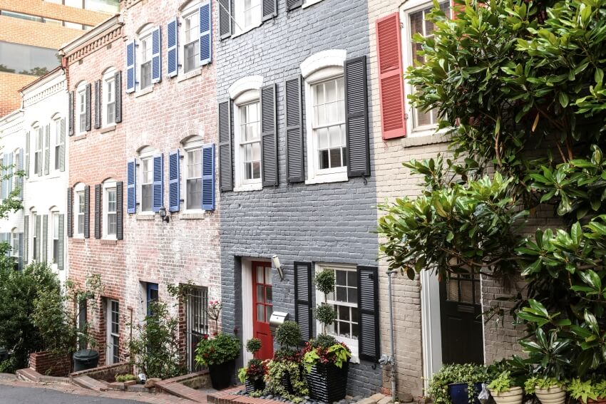 A quaint row of townhouses with painted brick exteriors, and windows with exterior shutters