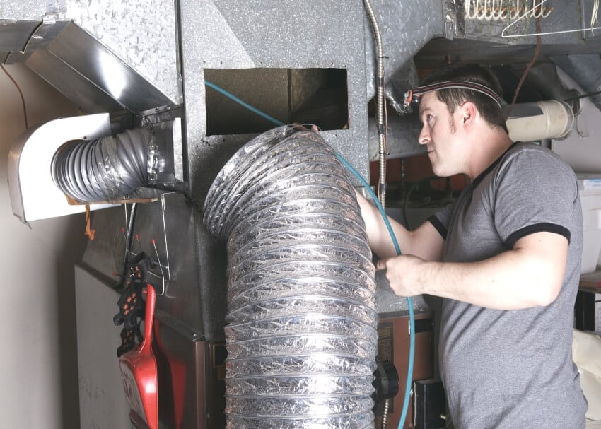 A ventilation cleaner man at cleaning the duct furnace with a tool
