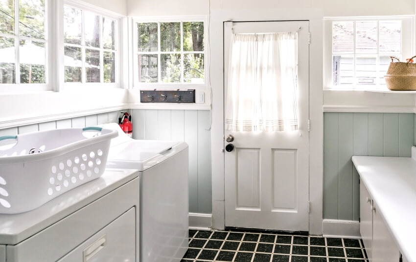 A vintage laundry room with windows and natural light, a washer, dryer, and a laundry basket