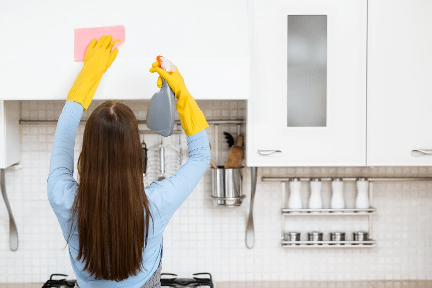 A woman in yellow gloves cleaning the laminate kitchen cabinet with a spray detergent