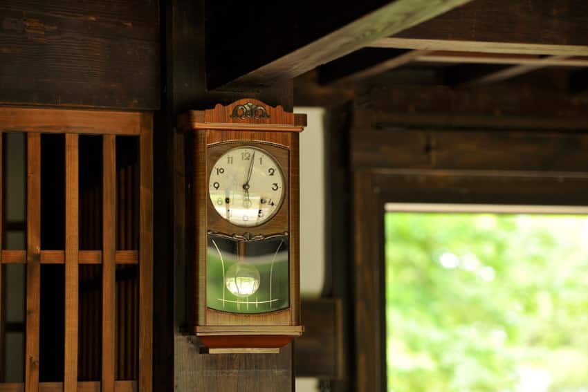 Analog clock with pendulum on wood wall