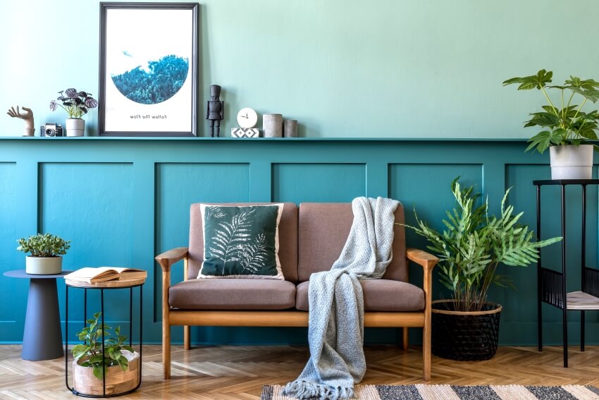 Apartment living room with brown sofa, plants, end table, poster frames, and blue wood paneling