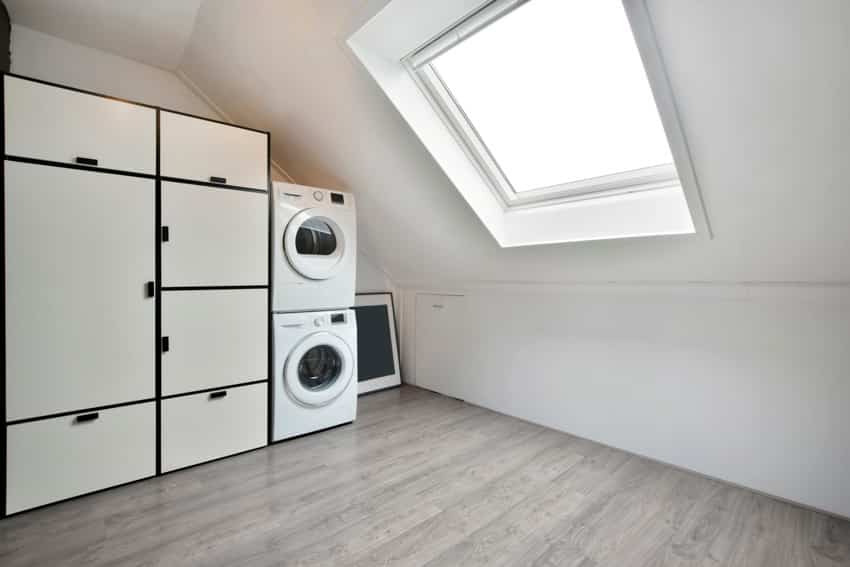 Attic laundry room with stackable washer dryer, skylight, window, and cabinets