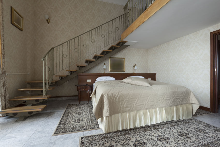 Basement bedroom with staircase, floor rug, and bedsheets