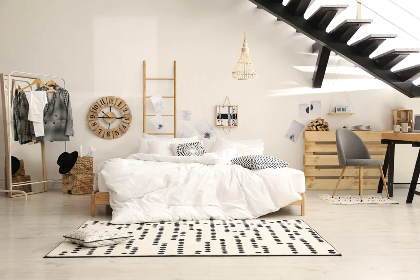 Basement bedroom with table, chair, floor, rug, bedsheets, and white wall