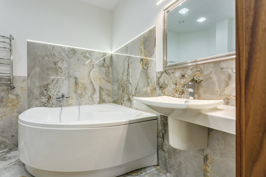 Bathroom with acrylic tub, marble wall, mirror, and sink